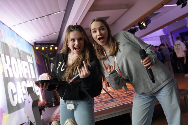 Zwei M&auml;dchen auf dem KonfiCastle zeigen eine Handgeste (Zeige- und kleiner Finger erhoben), um ihre Begeisterung auszudr&uuml;cken.